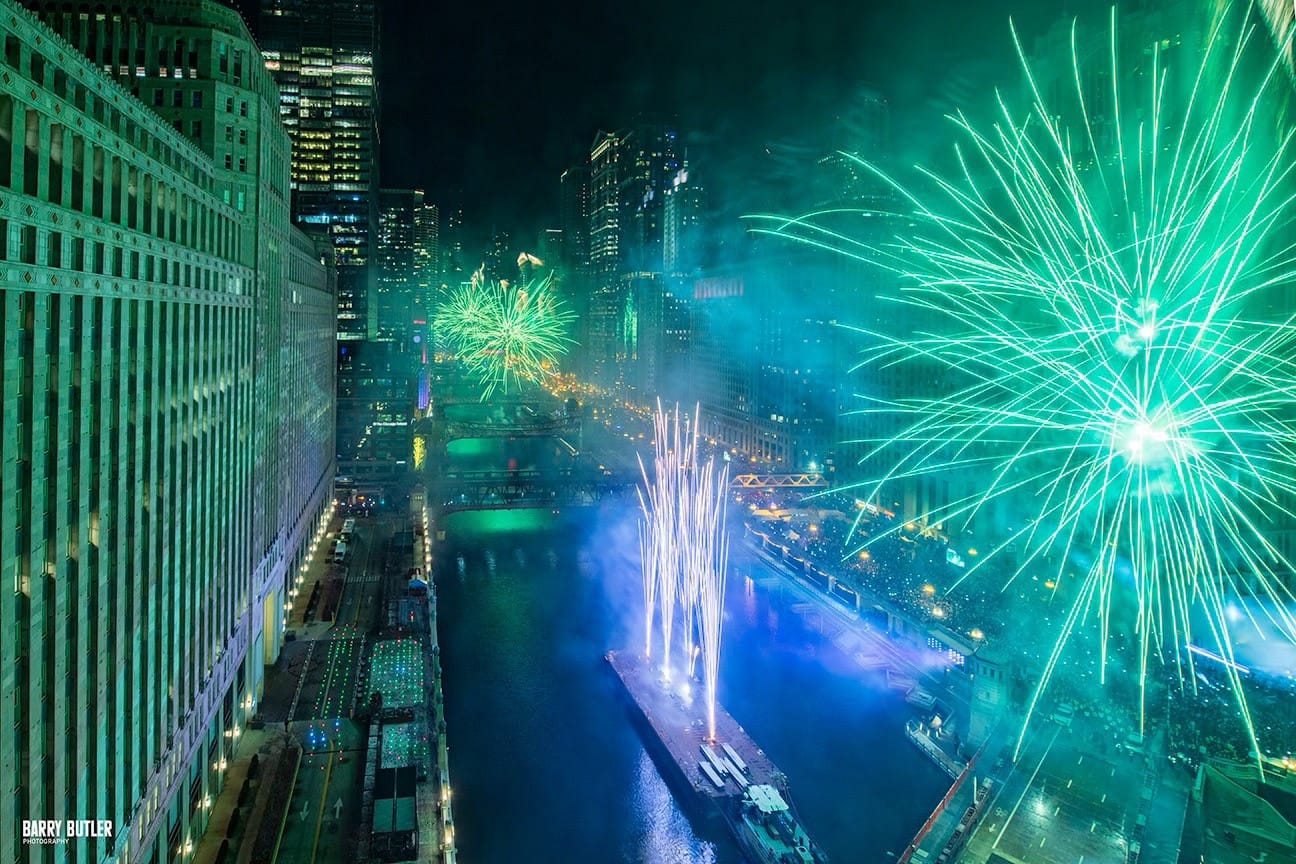 Green NYE fireworks light up the Chicago River and surrounding buildings.